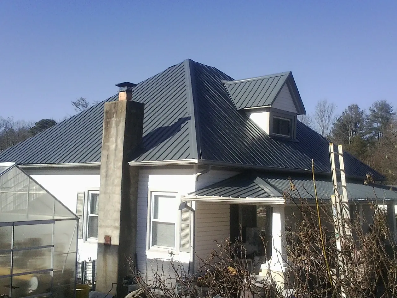 Dark blue standing seam metal roof on a white farmhouse with dormer — Slate & Tile Roof Repair by Roofing Brothers in Winburne