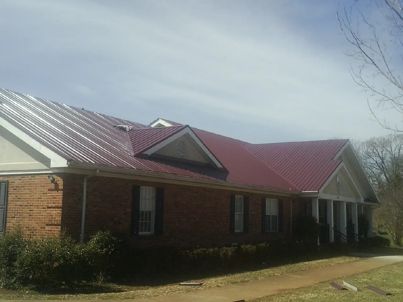 Red metal roof with gabled entries on a long brick building, from a Hail Damage Roof Repair job in Winburne