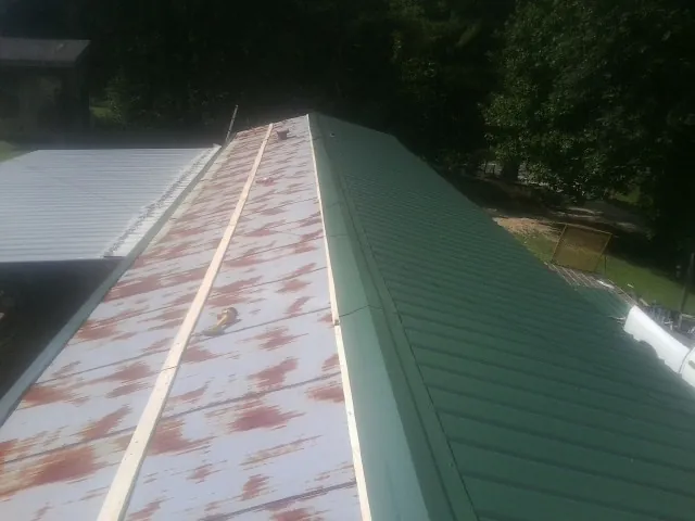 Old rusted panels beside newly installed green metal roofing — Wind Damage Roof Repair by Roofing Brothers in Winburne